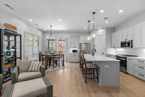 Kitchen with a breakfast bar area, an island with sink, appliances with stainless steel finishes, hanging light fixtures, and gray cabinets