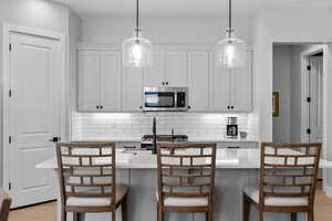 Kitchen featuring tasteful backsplash, light wood-type flooring, stainless steel microwave, and pendant lighting