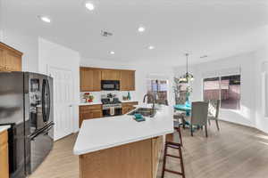 Kitchen with black appliances, light wood-type flooring, brown cabinets, hanging light fixtures, and recessed lighting