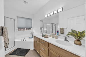 Full bathroom with a stall shower, double vanity, a garden tub, and light wood-type flooring