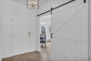 Entryway with a barn door, wood finished floors, and a chandelier
