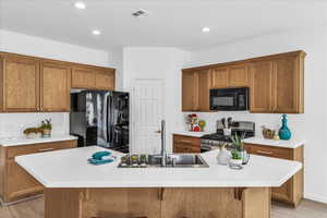 Kitchen with light wood-type flooring, brown cabinets, black appliances, a breakfast bar, and recessed lighting