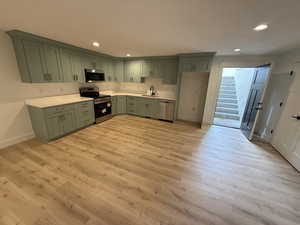 Kitchen with appliances with stainless steel finishes, green cabinets, recessed lighting, and light wood-style flooring