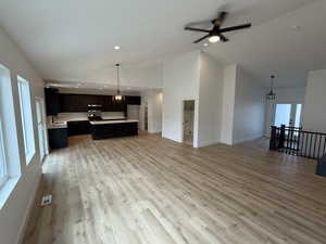 Unfurnished living room featuring light wood finished floors, a chandelier, a ceiling fan, high vaulted ceiling, and recessed lighting