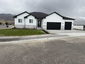 Modern farmhouse style home with a front yard, driveway, stone siding, board and batten siding, and a shingled roof