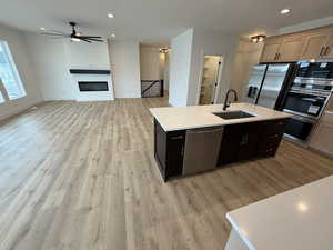 Kitchen featuring recessed lighting, stainless steel appliances, a center island with sink, light wood-type flooring, and a glass covered fireplace