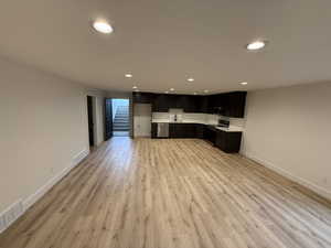 Kitchen with light countertops, recessed lighting, stainless steel appliances, light wood finished floors, and dark cabinetry