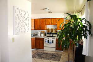 Kitchen with white electric range, light tile patterned flooring, light countertops, and brown cabinetry