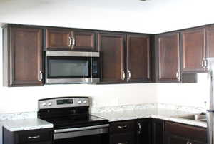 Kitchen featuring stainless steel appliances, dark brown cabinets, and light stone counters