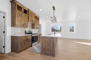 Kitchen with stainless steel range with electric cooktop, brown cabinets, pendant lighting, a center island with sink, and backsplash