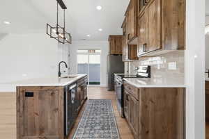 Kitchen with appliances with stainless steel finishes, an island with sink, decorative light fixtures, light wood finished floors, and brown cabinets