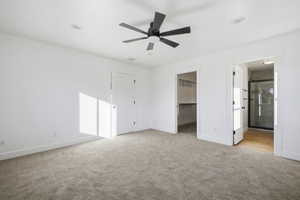 Unfurnished bedroom with ceiling fan, a walk in closet, and light colored carpet