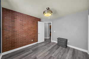 Empty room featuring brick wall and dark wood-type flooring