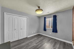 Unfurnished bedroom with wood finished floors, a closet, and a textured ceiling