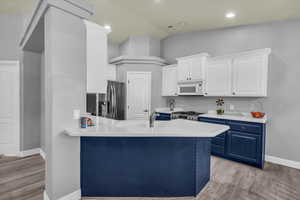 Kitchen with blue cabinetry, appliances with stainless steel finishes, white cabinetry, light wood-style flooring, and vaulted ceiling