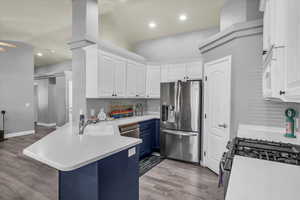 Kitchen featuring blue cabinets, a peninsula, white cabinetry, appliances with stainless steel finishes, and light wood-style floors