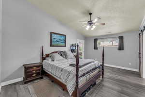 Bedroom with a barn door, vaulted ceiling, wood finished floors, a textured ceiling, and a ceiling fan