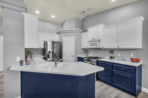 Kitchen with blue cabinetry, light wood finished floors, a peninsula, and recessed lighting