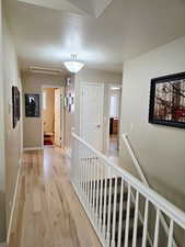 Corridor with an upstairs landing, a textured ceiling, and light wood-type flooring