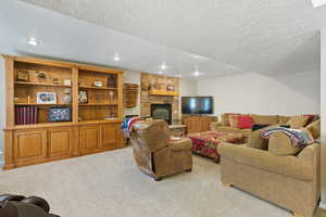Carpeted living area with a textured ceiling, a stone fireplace, and recessed lighting