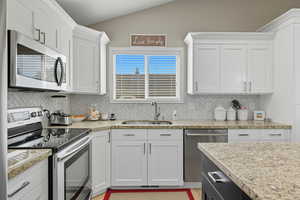 Kitchen featuring stainless steel appliances, white cabinetry, backsplash, and lofted ceiling