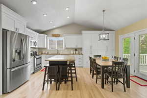 Kitchen with stainless steel appliances, lofted ceiling, pendant lighting, white cabinetry, and decorative backsplash