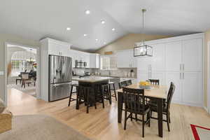 Dining room with a chandelier, light wood finished floors, vaulted ceiling, recessed lighting, and healthy amount of natural light