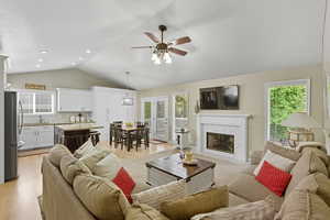 Living room with lofted ceiling, plenty of natural light, a tile fireplace, ceiling fan, and light wood-type flooring
