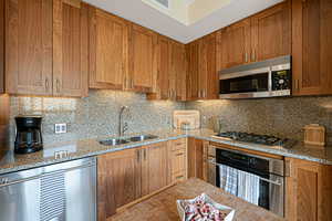 Kitchen featuring appliances with stainless steel finishes, backsplash, walnut cabinets, and light stone countertops