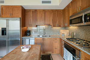 Kitchen featuring appliances with stainless steel finishes, tasteful backsplash, walnut cabinets, light stone counters, and light wood finished floors