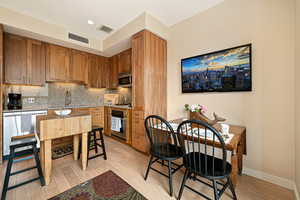 Kitchen featuring tasteful backsplash, walnut cabinetry, light wood-type flooring, appliances with stainless steel finishes, and recessed lighting