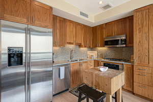 Kitchen with appliances with stainless steel finishes, walnut cabinetry, light stone counters, decorative backsplash, and recessed lighting