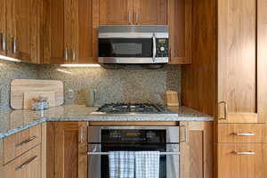 Kitchen featuring stainless steel appliances, tasteful backsplash, walnut cabinets, and light stone counters