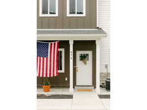 Entrance to property featuring board and batten siding, a porch, roof with shingles, and stone siding