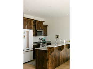 Kitchen featuring high end appliances, dark brown cabinets, light wood-style floors, light stone countertops, and a kitchen bar