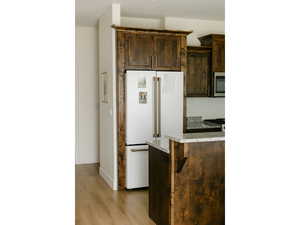 Kitchen featuring dark brown cabinetry, freestanding refrigerator, light stone counters, and light wood-type flooring