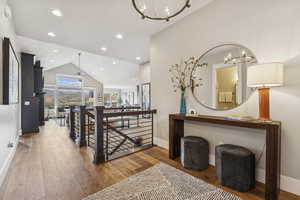 Hall with an upstairs landing, a chandelier, hardwood / wood-style floors, recessed lighting, and high vaulted ceiling