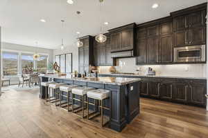 Kitchen with backsplash, a kitchen breakfast bar, hanging light fixtures, light stone counters, and recessed lighting
