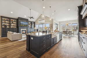 Kitchen featuring light stone counters, hanging light fixtures, recessed lighting, dark wood-type flooring, and a glass covered fireplace