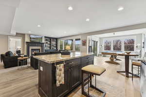 Kitchen with open floor plan, light stone countertops, light wood-style flooring, recessed lighting, and a stone fireplace