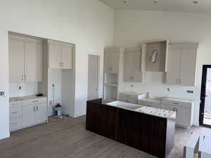 Kitchen with high vaulted ceiling, a kitchen island, wood finished floors, white cabinetry, and dark brown cabinetry