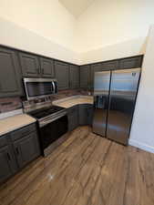 Kitchen with gray cabinetry, stainless steel appliances, light countertops, dark wood finished floors, and backsplash