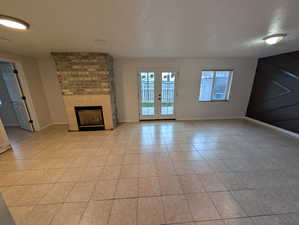 Unfurnished living room featuring a fireplace, light tile patterned flooring, and french doors