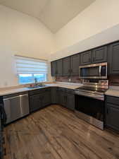 Kitchen featuring gray cabinetry, appliances with stainless steel finishes, lofted ceiling, light countertops, and dark wood finished floors