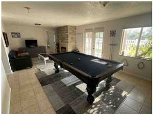 Game room featuring pool table, french doors, a textured ceiling, a fireplace, and light tile patterned floors