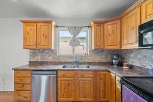 Kitchen with black appliances, dark countertops, backsplash, and brown cabinetry