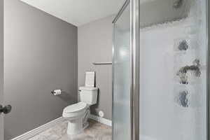 Bathroom with a textured ceiling, a stall shower, and light tile patterned floors