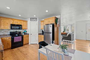 Kitchen featuring black appliances, decorative backsplash, light wood finished floors, recessed lighting, and dark countertops
