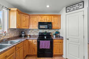 Kitchen with black appliances, backsplash, light wood-type flooring, dark countertops, and recessed lighting