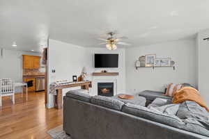 Living room with a warm lit fireplace, light wood-style flooring, a ceiling fan, and recessed lighting